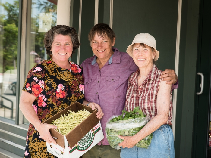 Three women holding produce and smiling at the camera